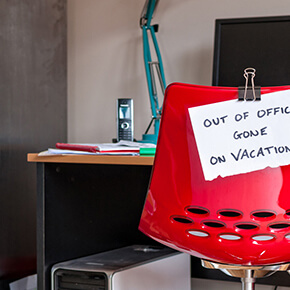 Unoccupied Red office chair at desk with sign saying out of office gone on vacation