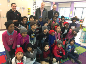 Partners, Sean Daughton and William Michalski and another guy with a group of children with hats for a hat and glove charity event
