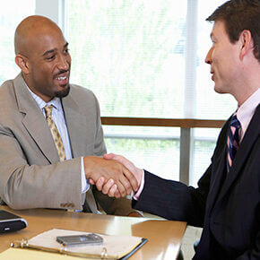 Two business men sitting at a table shaking hands