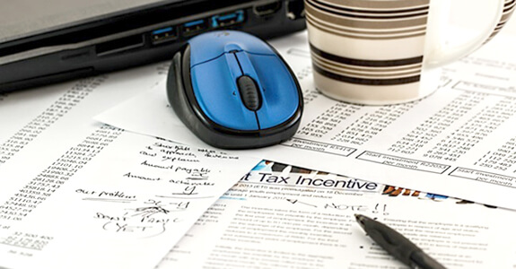 Financial papers on a desk with a blue mouse and stripped coffee mug with pen