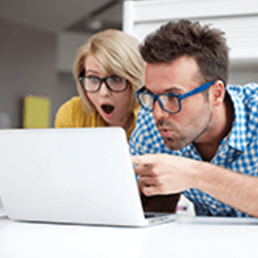 Lady with glasses and man with blue glasses looking happily surprised at something on a laptop