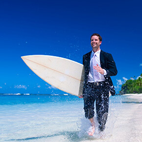 Man in suit with surfboard walking briskly on beach