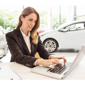 saleswoman on computer with new cars in background