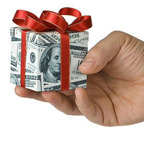 Hand holding gift box wrapped with 100 dollar bill with red bow