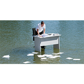 Man standing at a white desk in middle of water with papers scattered on water