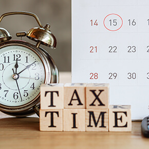 Wooden blocks spelling out "tax time" in front of a clock and calendar