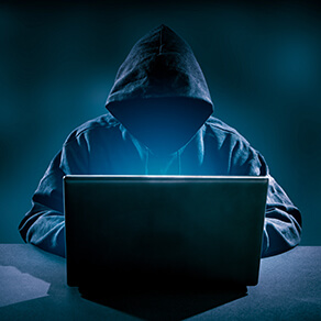 person in hooded jacket sitting in front of laptop hacking into it