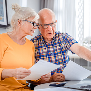 Worried senior couple checking bills using laptop and papers at home