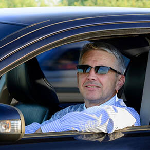 Man in drivers seat of car with windows down and wearing sunglasses