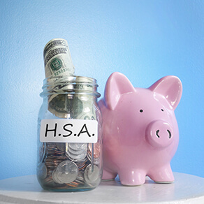 Jar with cash and coins with "H.S.A." on it next to pink piggy bank