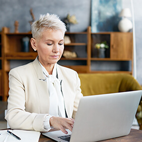 Lady with white suit and short gray hair typing on laptop