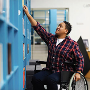 Person in wheelchair reaching for object on high shelf