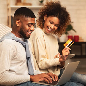 Couple sitting together on computer, woman is holding a credit card