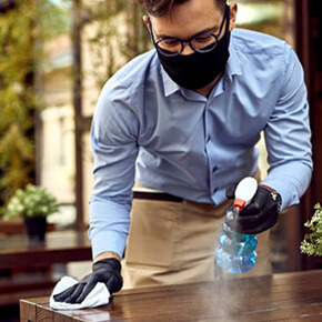 Waiter spraying and wiping down a table