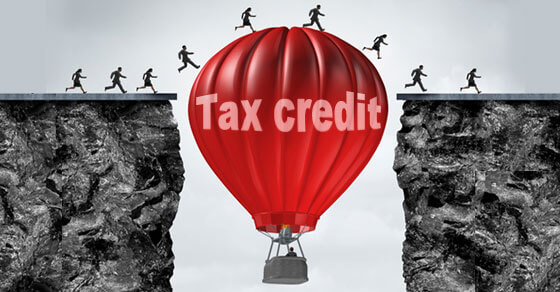 Red hot air balloon with words tax credit between two cliffs with people running over the top