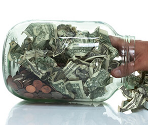 Clear jar stuffed with dollar bills and pennies and hand reaching in to grab some