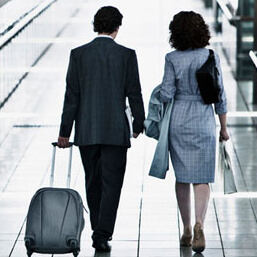 Back of business man and woman walking through airport with man pulling luggage