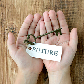 Hands cupped over a wood table holding an antiques key with a tag that reads future.