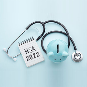 Doctor’s stethoscope wrapped around a notepad with the words “HSA 2022 on it,” and a blue piggy bank