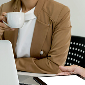 Women holding a coffee cup sitting in front of a laptop