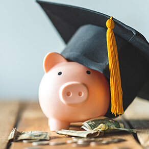 Pink piggy bank with graduation hat on and dollar bills laying next to it