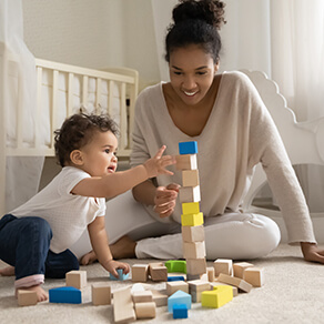 Woman in front of crib playing with blocks with baby