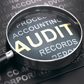 Magnifying glass with focus on the word audit written in golden letters and other accounting words over black background