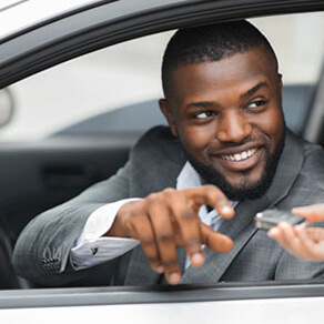 Man in a car leaning out of the window with a hand giving him a key