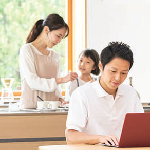 Man at his laptop with a woman and child at a desk behind him