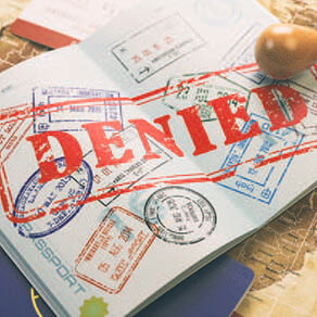 Open passport with a large, bright red “Denied” stamp in the middle.