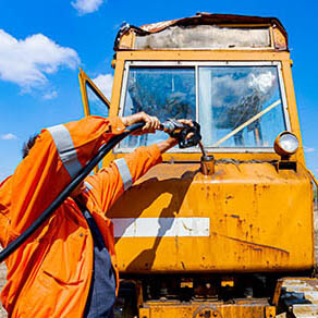 Worker holding fuel pump gun inserted in the reservoir of construction machine, pour gasoline, diesel in the vehicle.