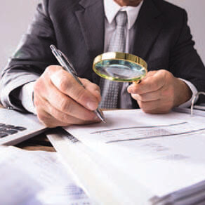 Man with magnified glass looking at documents and taking notes