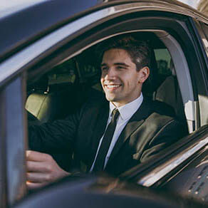 Side profile view smiling young driver smiling businessman man 20s wear black dinner suit driving car taxi hold steering wheel look camera Vehicle transport traffic lifestyle business trip concept