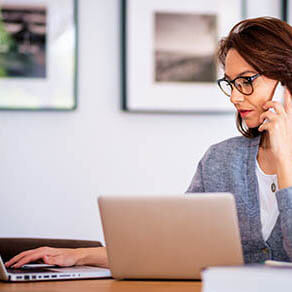 Woman sitting at home and using laptops and having a call. Confident female wearing casual clothes and glasses. Home office.