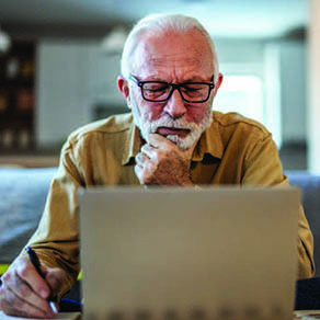 Older man looking closely at a computer screen with his hand resting on his chin