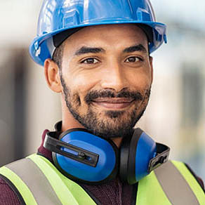 Portrait of happy construction site manager wearing safety vest and blue helmet.